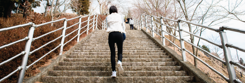 Woman climbing stairs along a trail through a park to get in more steps.