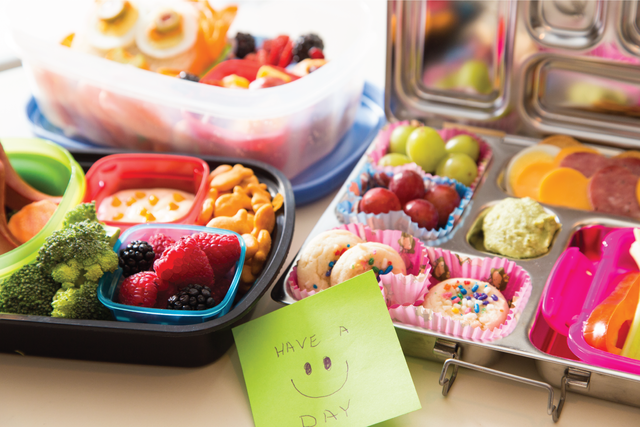 A note that reads “have a happy day” sits in front of several packed lunches.