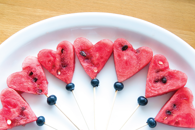  Pieces of heart-shaped watermelon on a spear with a blueberry accent underneath as part of a healthy school lunch