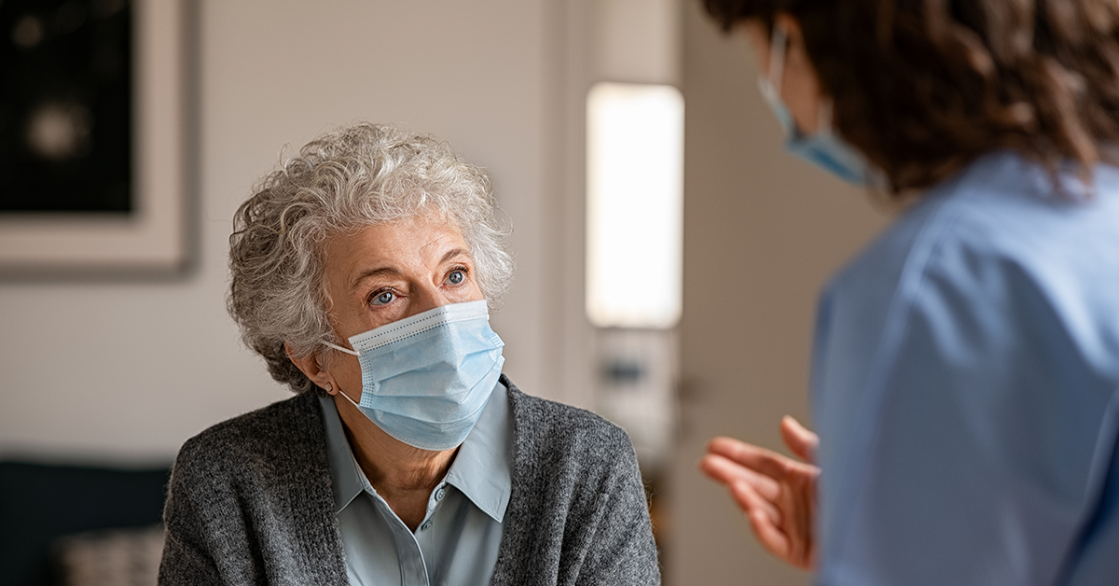 An older woman with a mask on listens to her nurse navigator talk about the WATCHMAN procedure for AFib.