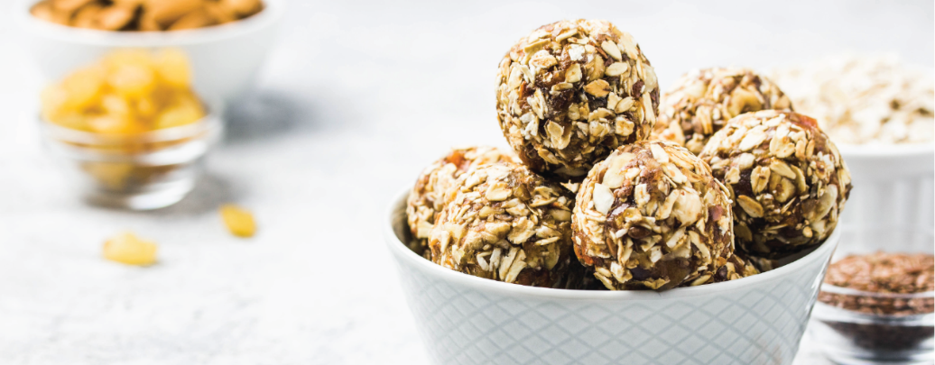 A bowl of no-bake protein balls made with oats, flaxseeds, and chocolate chips sits on a table.
