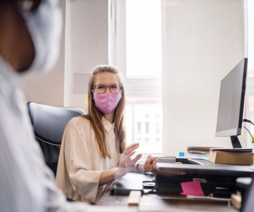 Two young women discuss workplace health tips while practicing social distancing and wearing masks.