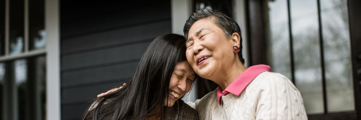 A senior woman and her adult child sit on the porch and laugh together.