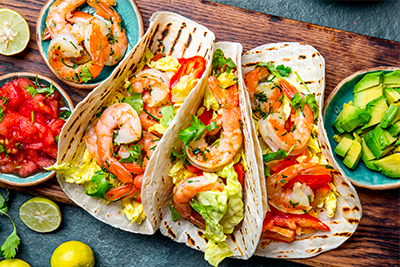 Spicy shrimp tacos topped with lettuce, avocados, tomatoes, lime juice, and cilantro, a delicious recipe for Lent